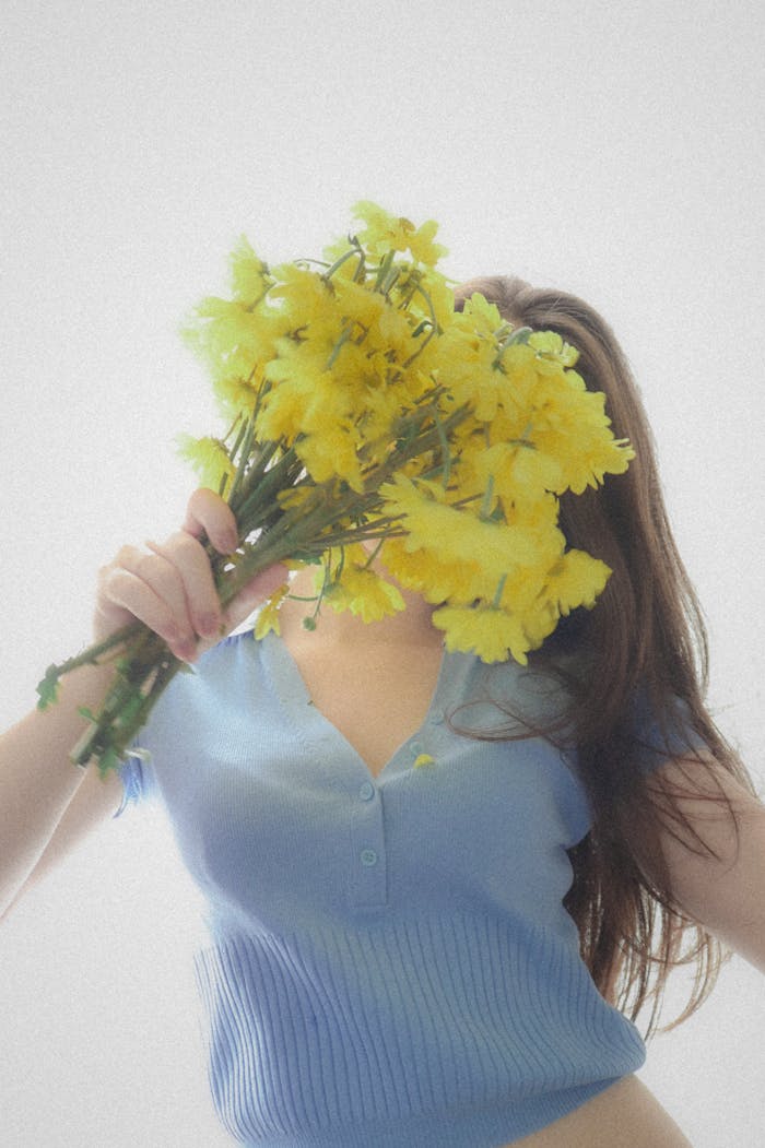 Woman in a blue shirt holding a bouquet of yellow flowers against a light background.