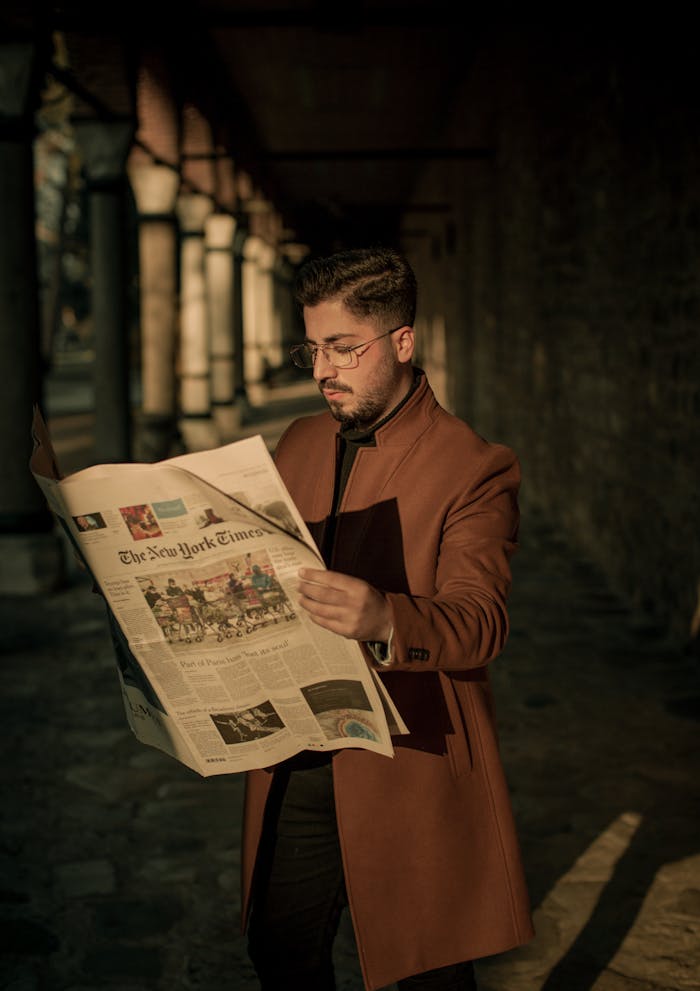 Stylish man reading The New York Times in a city alleyway during sunset.