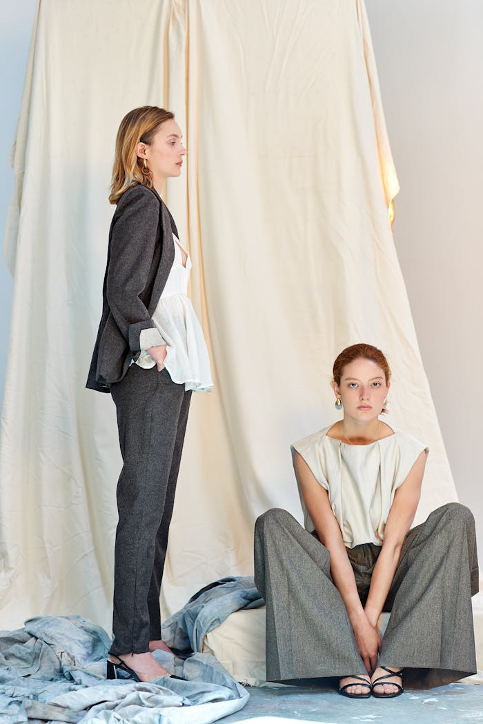 Elegant portrait of two women showcasing modern fashion in a minimalist studio setting.